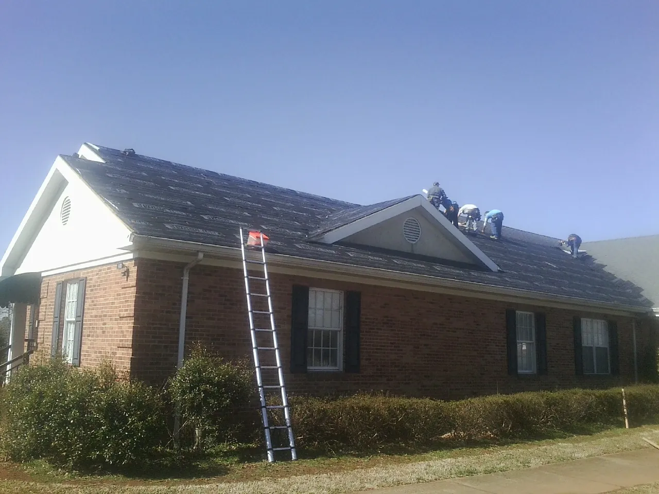 Crew tearing shingles off a brick ranch roof with a ladder set — Emergency Roof Repair work by our crew in Dry Run