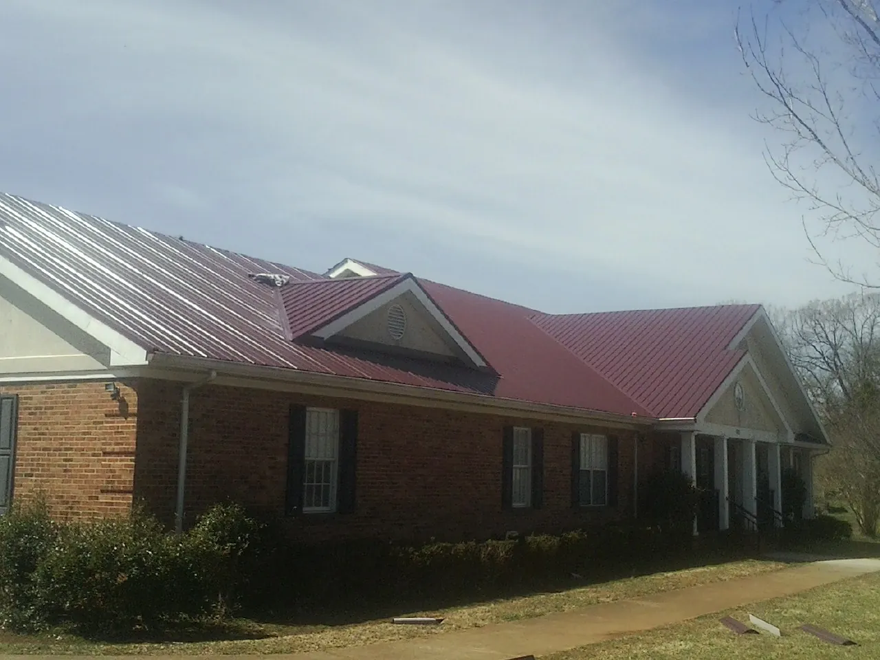 Red metal roof with gabled entries on a long brick building, from a Hail Damage Roof Repair job in Dry Run