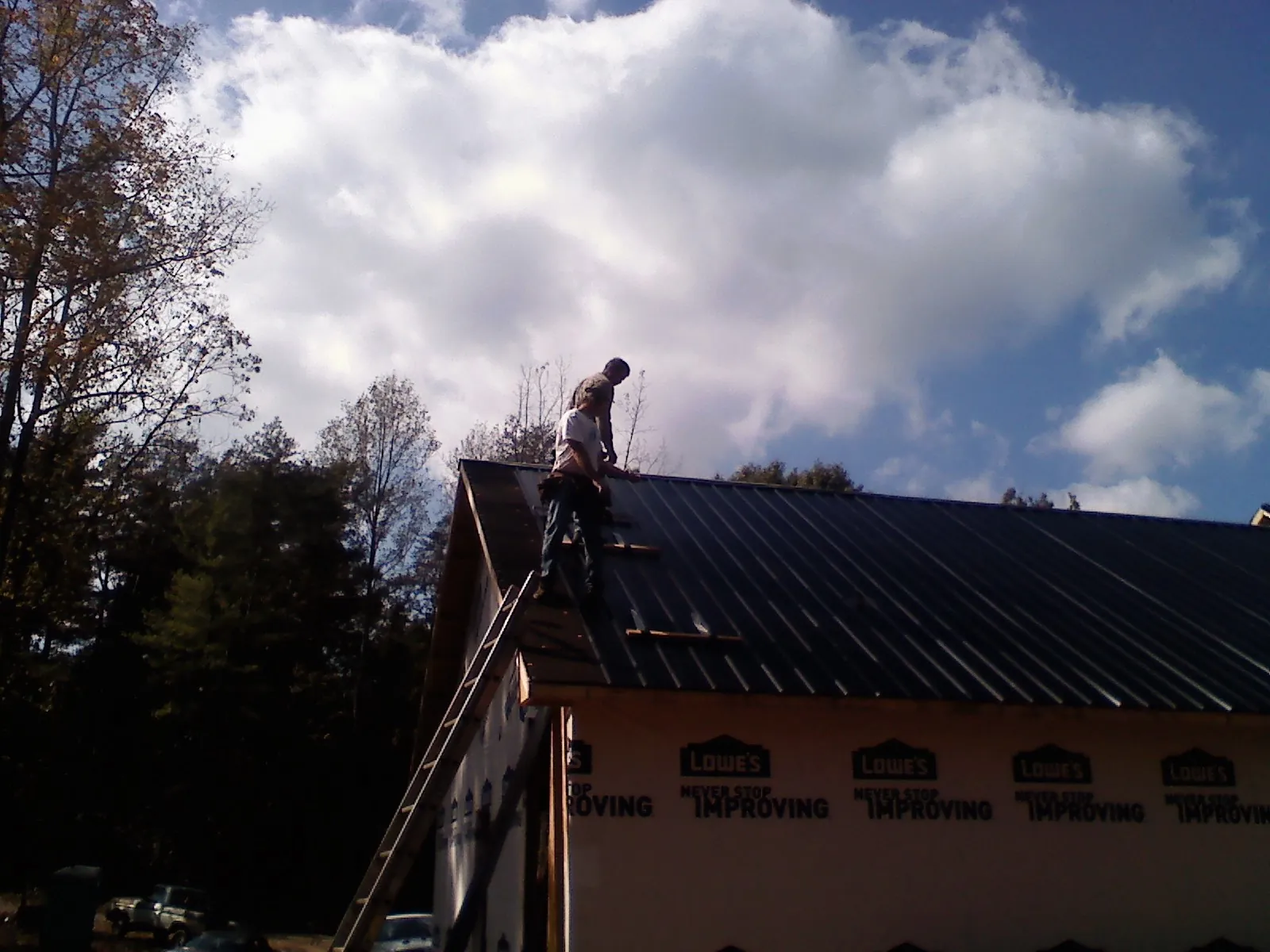 Roofer fastening dark metal panels high against a cloudy sky, from a Roof Inspection job in Dry Run