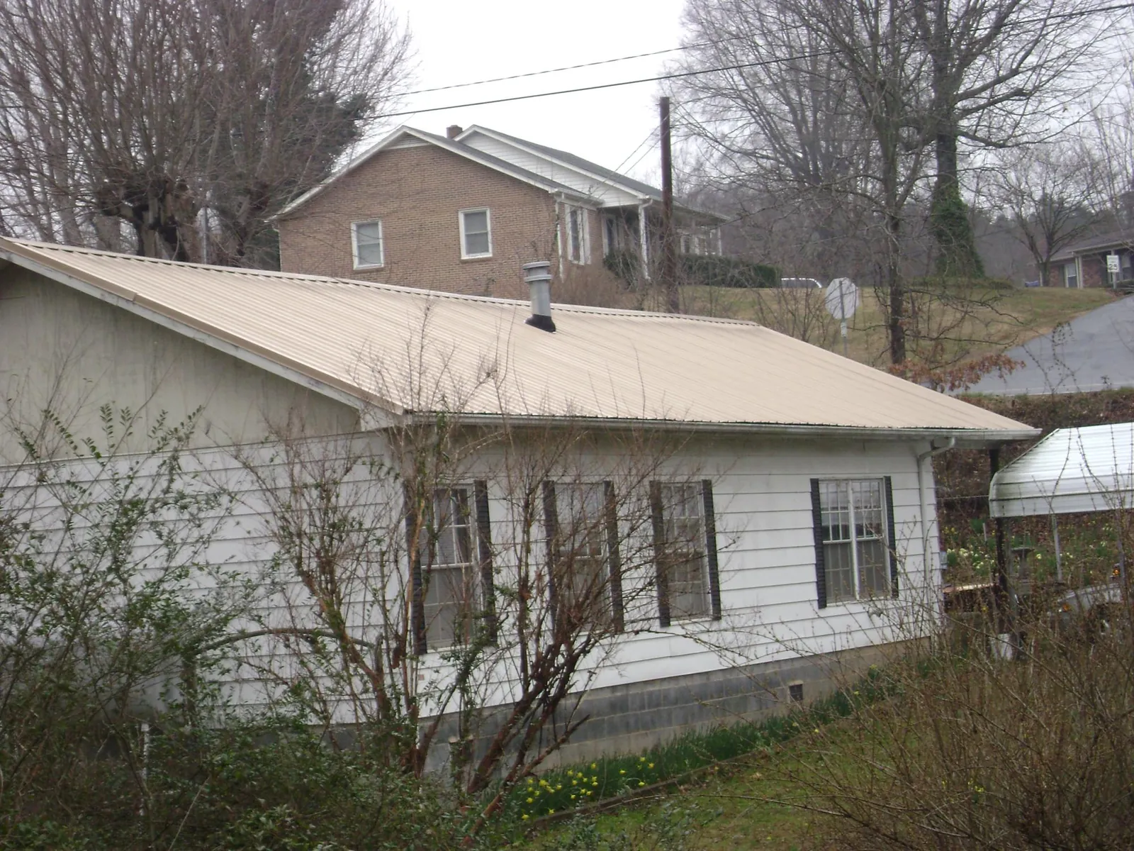 Tan metal roof on a white sided house set into a hillside — Commercial Roofing by Roofing Brothers in Dry Run